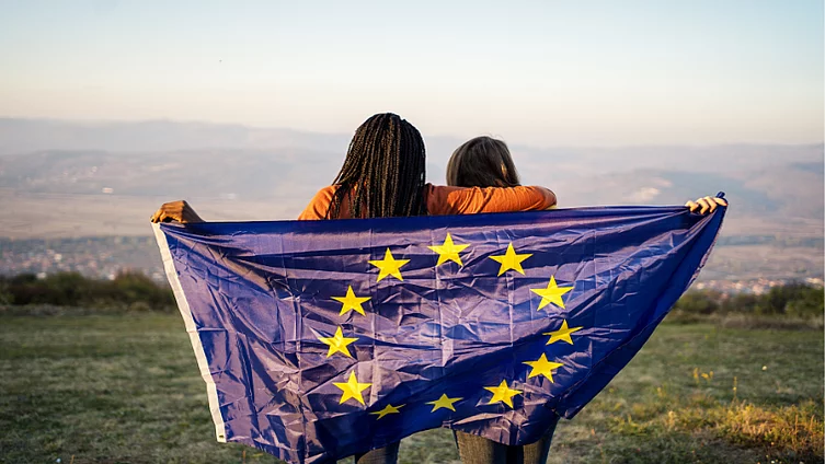 Two women with their backs turned to the camera holding up an EU flag.