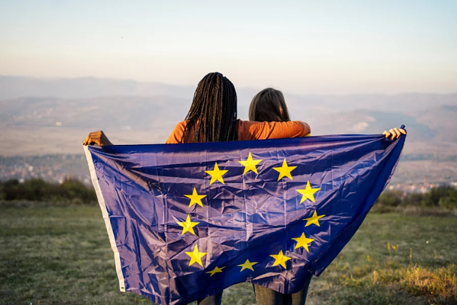 Two women with their backs turned to the camera holding up an EU flag.