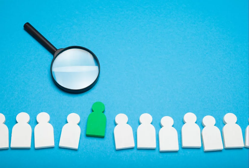 A row of white figures cut from paper and a green figure in the middle.
