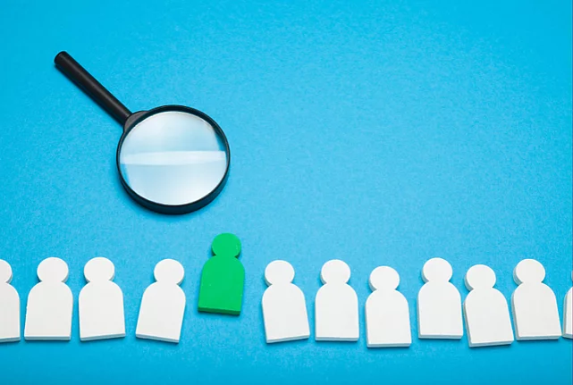 A row of white figures cut from paper and a green figure in the middle.
