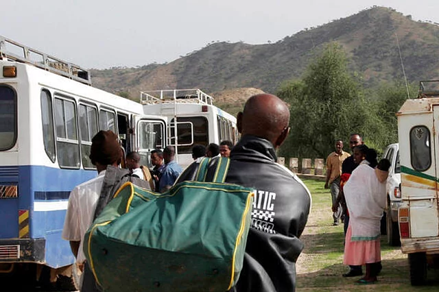 Repatriation of 232 Ethiopians across the Mereb Bridge: People with luggage waiting between busses and a blue UN sign.