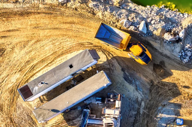 A mining site. Trucks are waiting on dusty ground beside a lake to pick up raw materials.