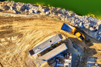 A mining site. Trucks are waiting on dusty ground beside a lake to pick up raw materials.